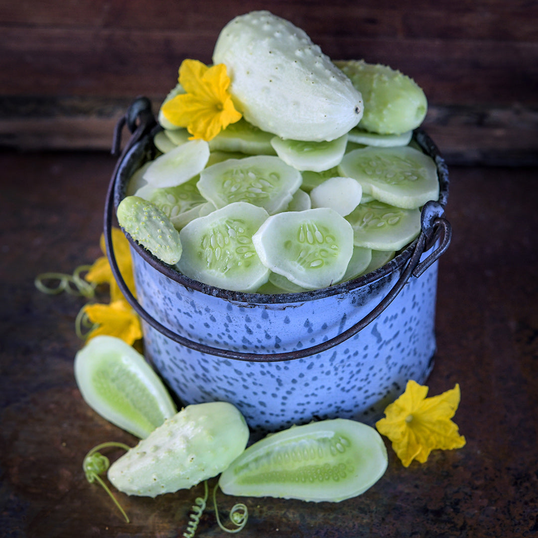 Sliced and whole Miniature White cucumbers in a small bucket on a dark background.