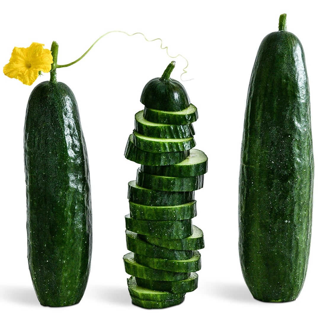 Two whole and one sliced Beit Alpha cucumber on a white background