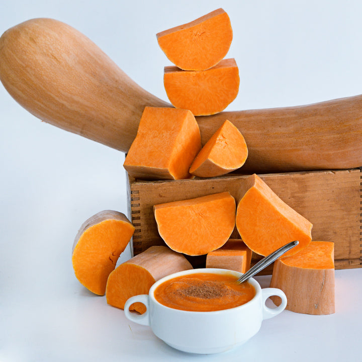 A closer view of cut and whole Long De Nice Winter Squash with a bowl of squash soup on white background.