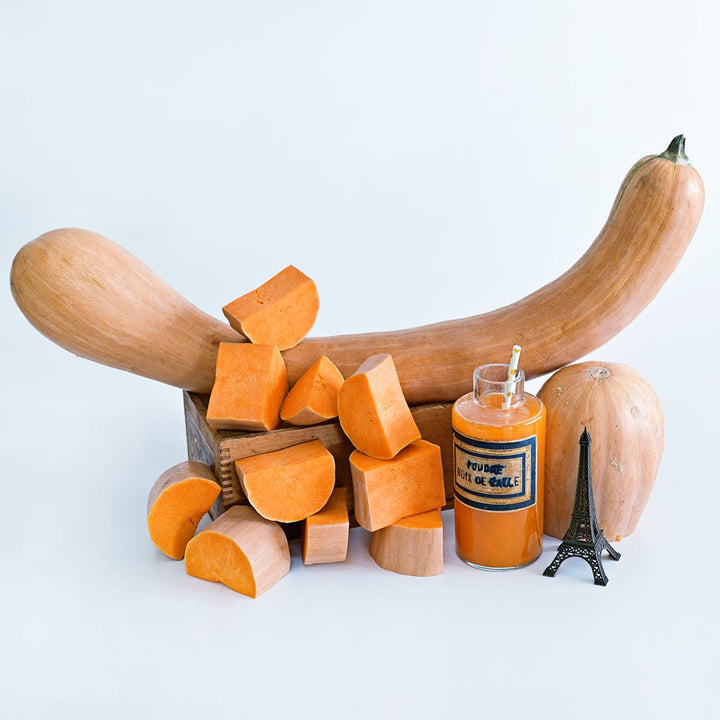 Cut and whole Long De Nice Winter Squash with squash juice and a miniature Eiffel Tower on white.