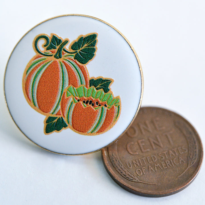 Baker Creek Kajari Melon Limited Edition Pin with a penny to show size on a white background.