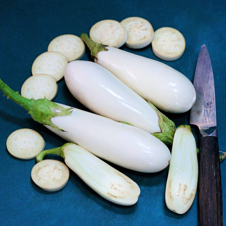 Cut and whole Casper Eggplant on teal background with a knife.