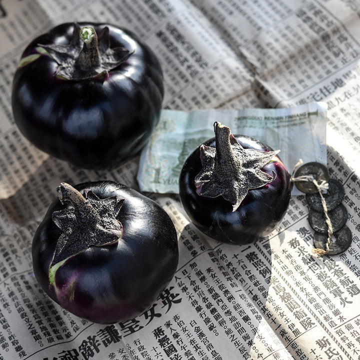 A trio of Qi Ye Round Eggplants on a Chinese newspaper with money and coins.