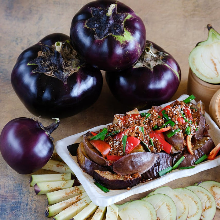 Cut and whole Qi Ye Round Eggplants with an authentic Chinese eggplant recipe on a white plate.