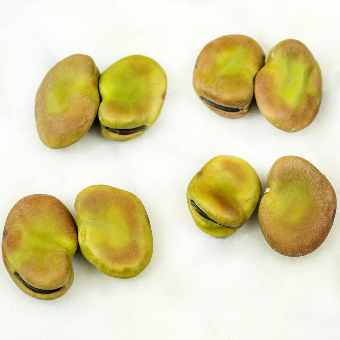 Four pairs of Masterpiece Fava Beans on a white marble background.