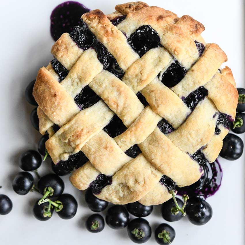 Garden Huckleberry pie with a few berries on the side on top of a white background