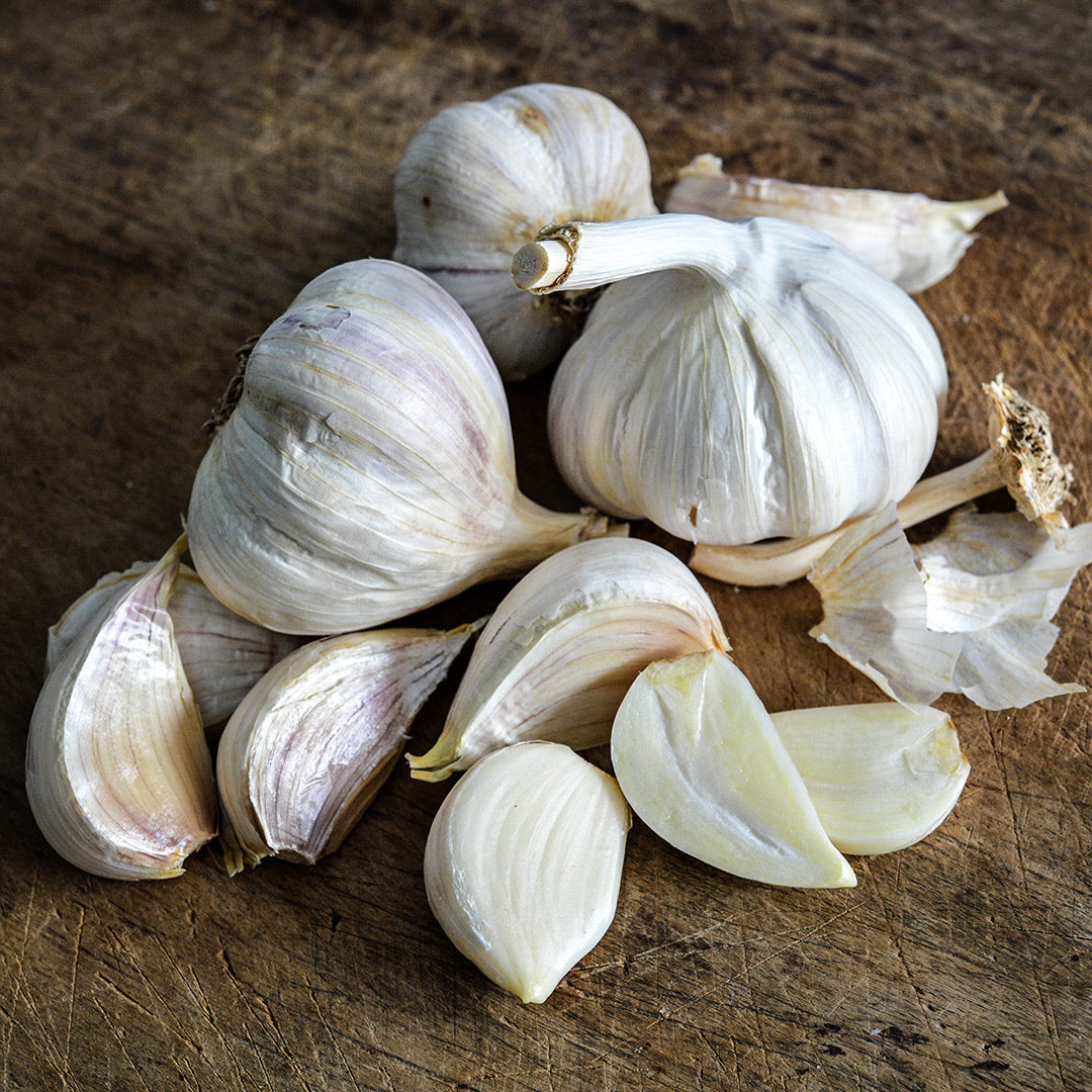 An arrangement of German Extra Hardy Garlic bulbs and cloves on a wooden cutting board.