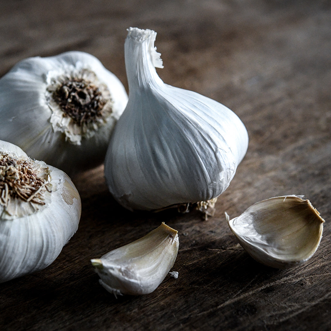 A close-up of Inchelium Red Garlic Bulbs and cloves on a wooden cutting board.