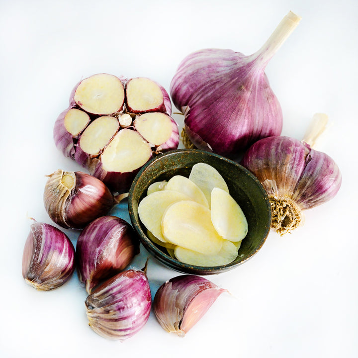 A bowl full of sliced Russian Inferno Garlic surrounded by bulbs and cloves on a white background.
