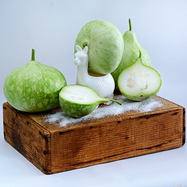 Cut and whole Peru Sugar Bowl Gourds with a white ceramic llama and sugar on wooden box.