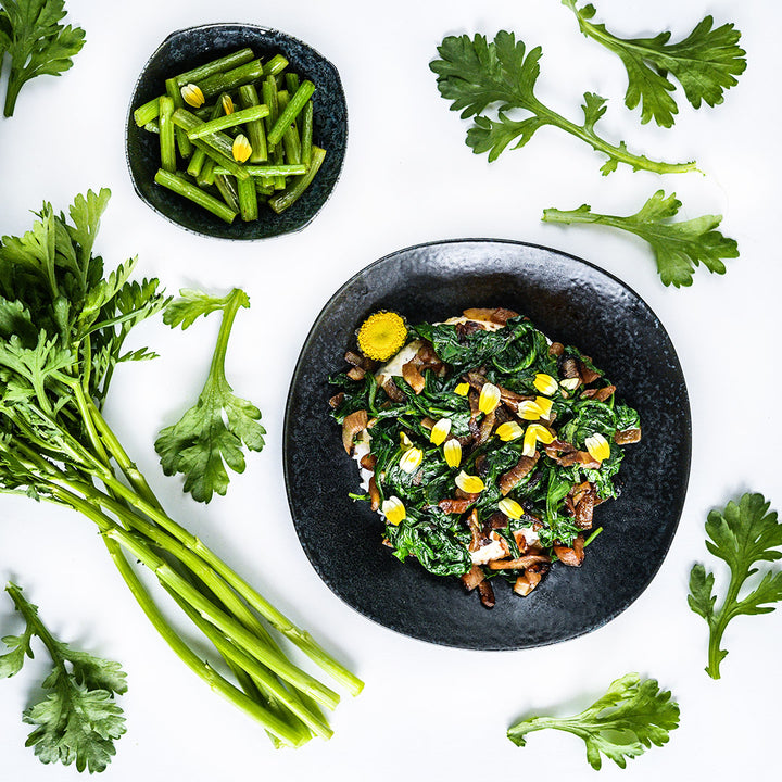 Cooked stems and greens from the Otafuku Chrysanthemum with fresh leaves on a white background.