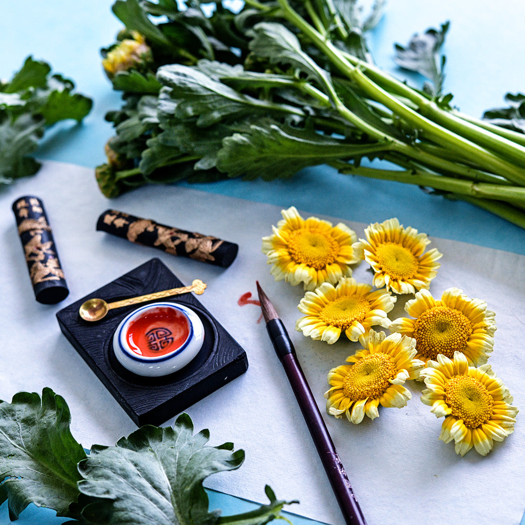 Otafuku Chrysanthemum greens stems and flowers arranged on a blue background.