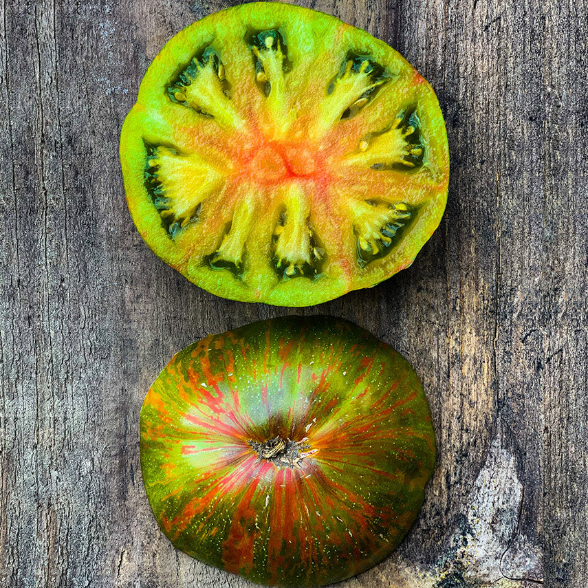 A halved Berkeley Tie-Dye Green Tomato showing both sides on wood. Image by Lucy Hutchins.