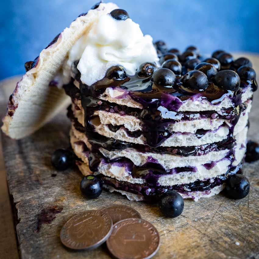 A stack of waffles with whipped cream on top smothered in Schwartzenbeeren berry syrup.