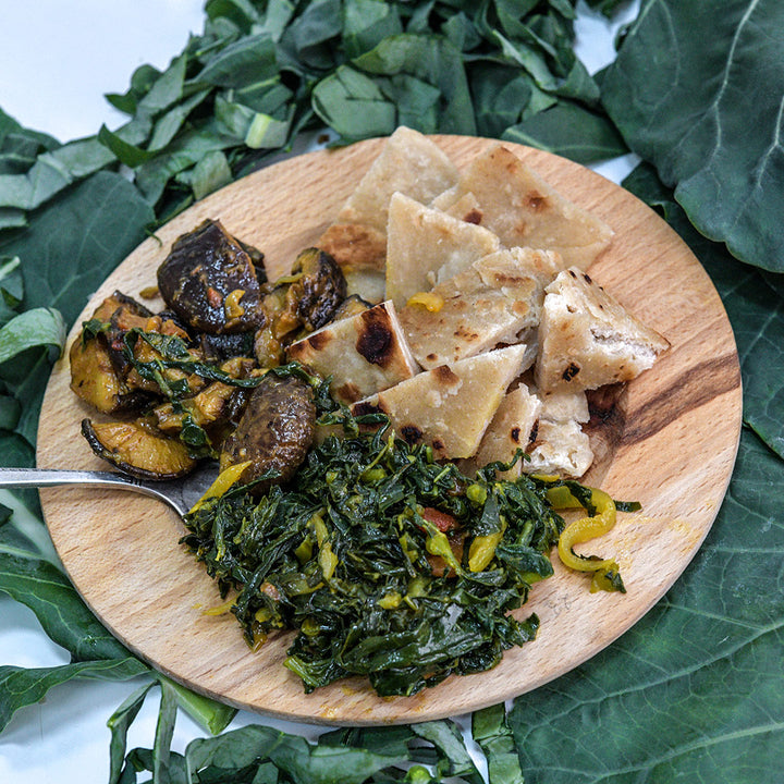 A wooden plate filled with African cuisine set on a bed of Sahara Kale leaves.