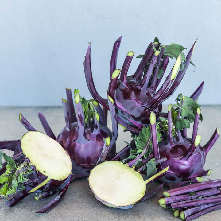 Several Blauer Speck Kohlrabi with one sliced open on a white background.