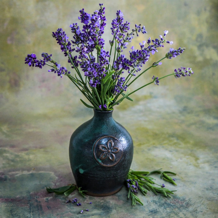 An arrangement of Ellagance Purple Lavender Handmade Mini Stoneware Bud Vase on a mottled green background.