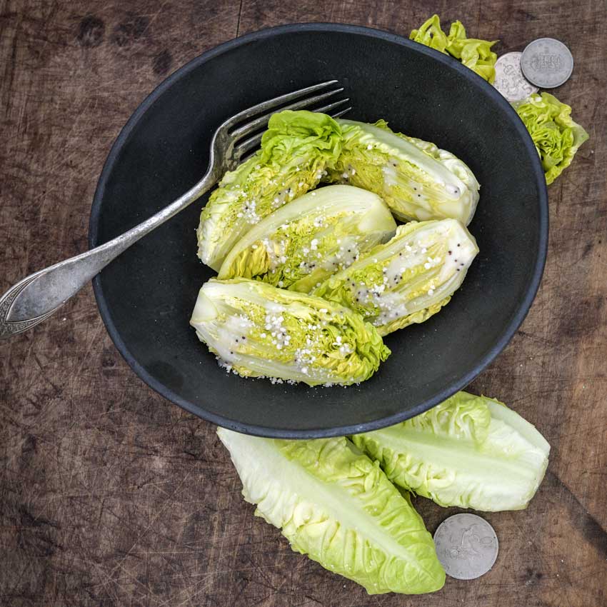 Little Gem Lettuce heads with dressing in a ceramic bowl on a wooden background.