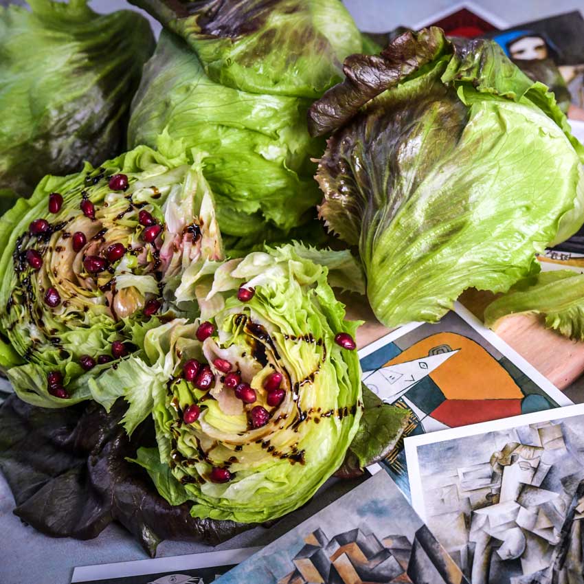 Three heads of Pablo Lettuce with one cut in half covered in dressing and pomegranate pearls.