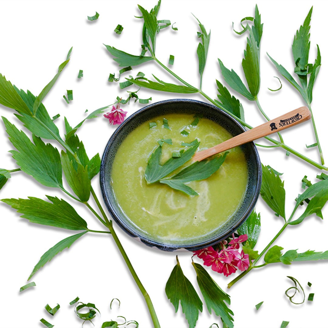 Lovage leaves in soup with phlox flowers on a white countertop.