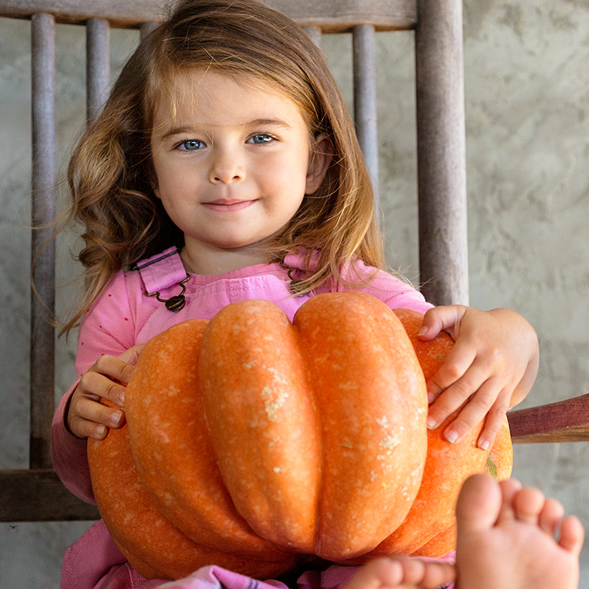 A smiling little girl holding a Moranga Winter Squash on her lap.