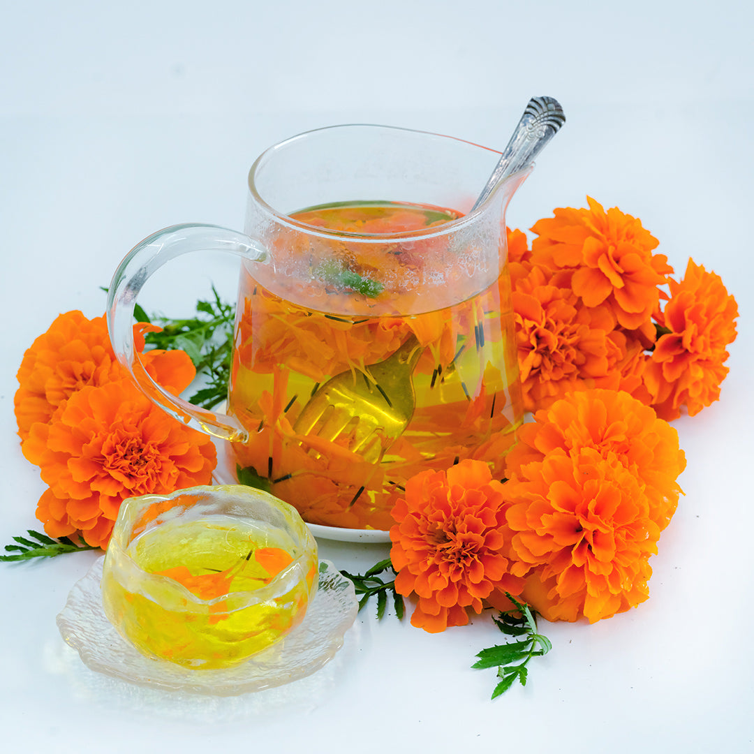 A clear glass pitcher full of Safari Tangerine Marigold tea with blooms on white background.