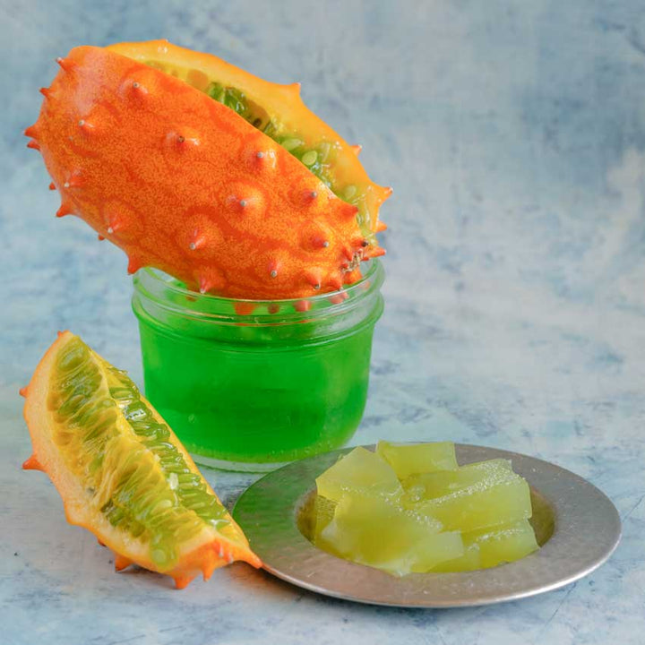 A Kiwano African horned jelly melon next to a plate and glass with melon gelatin on a light blue background.