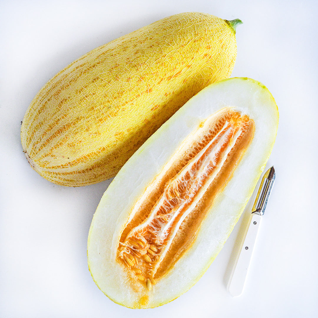 A cut and whole Tejen Giant Melon with a white handled peeler on a white background.