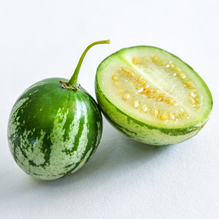 One whole and one half of Tzimbalo Melon Pears on a high key background.