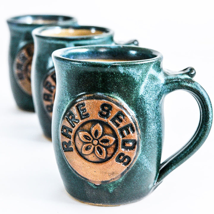 A trio of Handmade Green/Blue Stoneware Mugs with RareSeeds logo on a white background.
