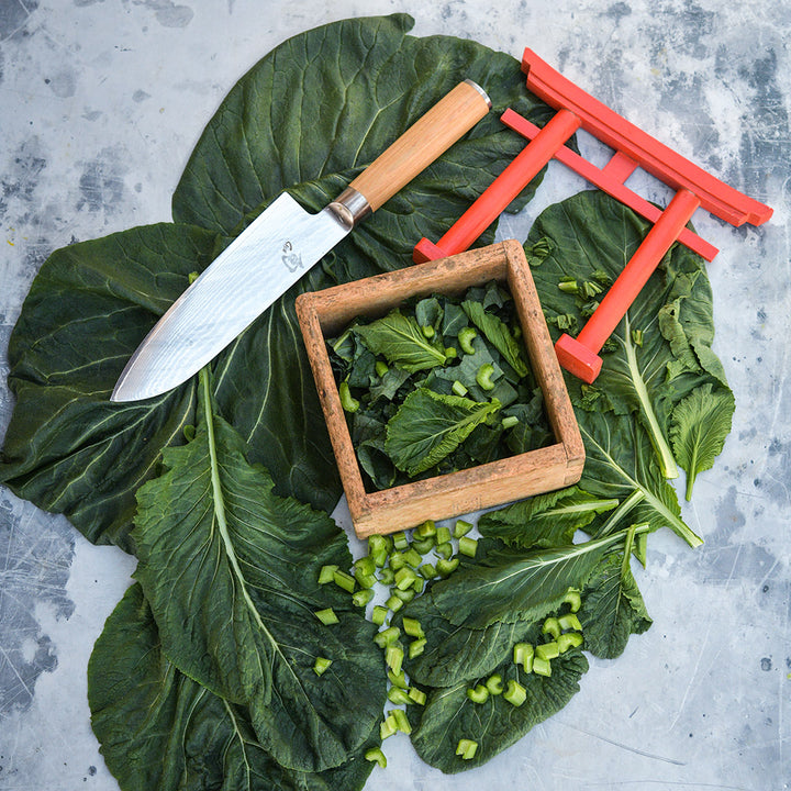 Large leaves from Spinach Mustard "Old Tokyo" Komatsuna with a large Japanese knife on a grey background.