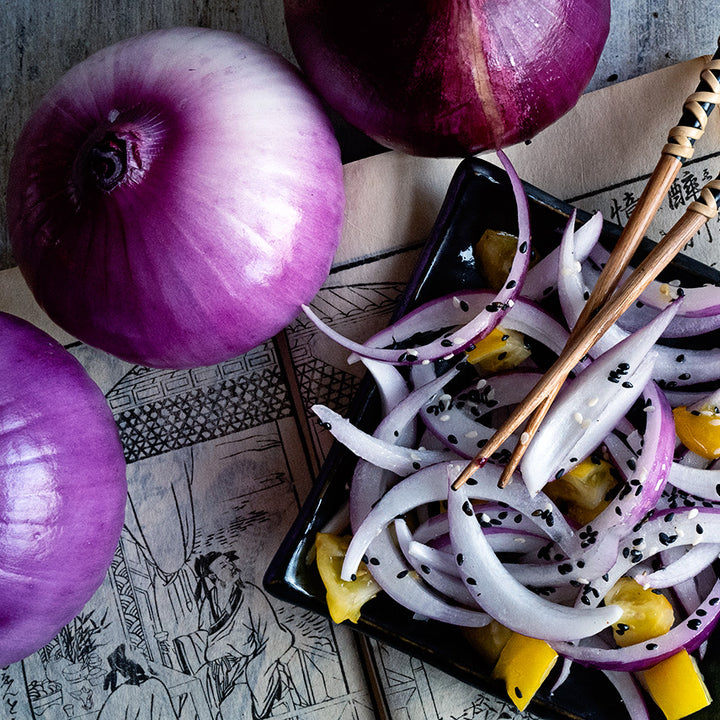 Close-up of whole Akatama Salad Red Onions with a plated onion salad and chopsticks.