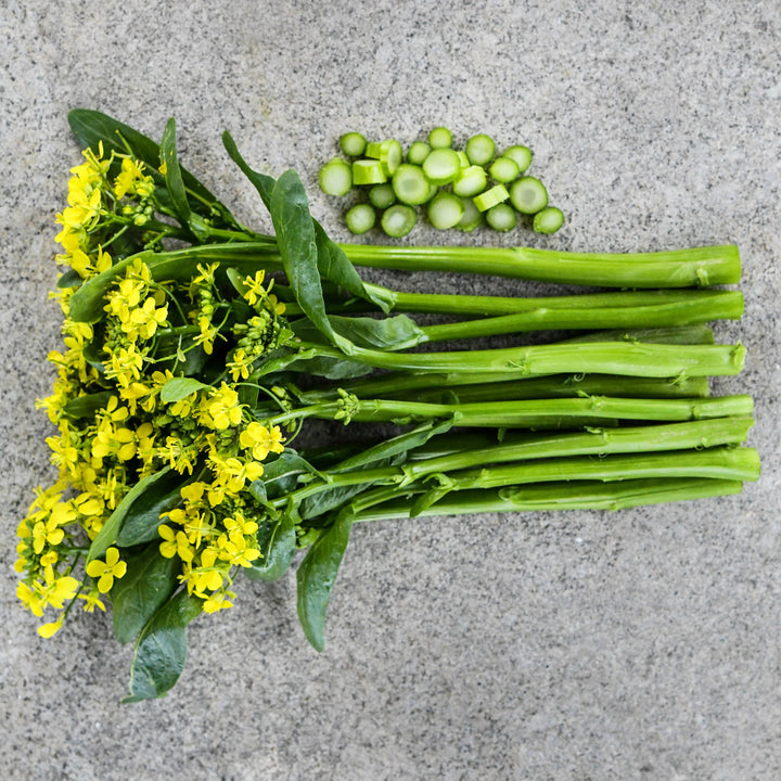 Blooming 50-Day Choy Sum stems with chopped stems on a stone background.