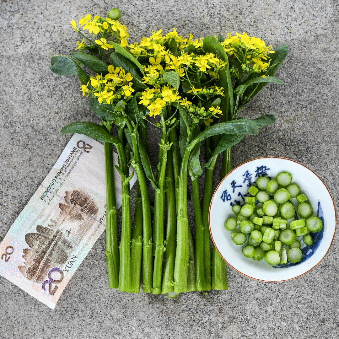Blooming 50-Day Choy Sum leaves with chopped stems in bowl and Chinese currency on a stone background.