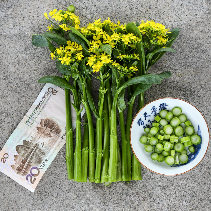 Blooming 50-Day Choy Sum leaves with chopped stems in bowl and Chinese currency on a stone background.