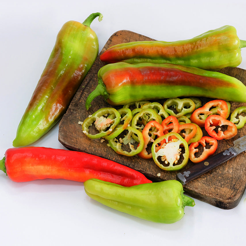 Whole and sliced Giant Aconcagua Sweet Peppers on wooden cutting board with a knife.