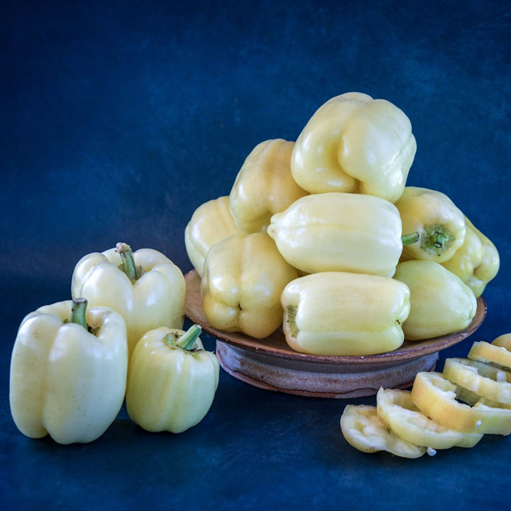 Albino Bull Nose Sweet Peppers in a ceramic bowl on a dark blue background.