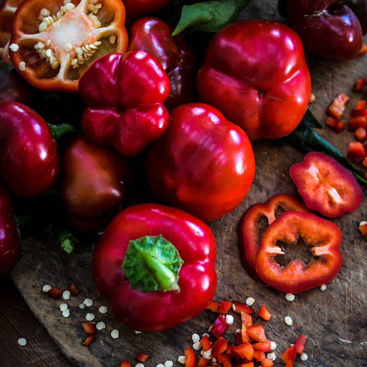 Several red Ashe County Pimiento Peppers in a rustic bowl wooden cutting board.