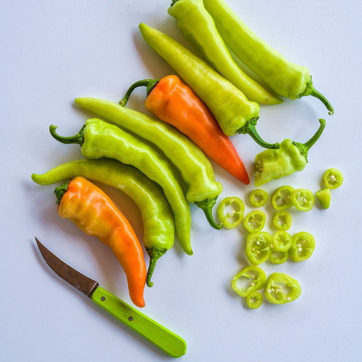 Banana Sweet Peppers with whole and sliced pieces next to a green-handled peering knife on a white background.