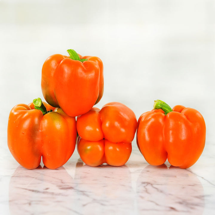 Four Orange Etiuda Sweet Peppers stacked up on a marble surface.