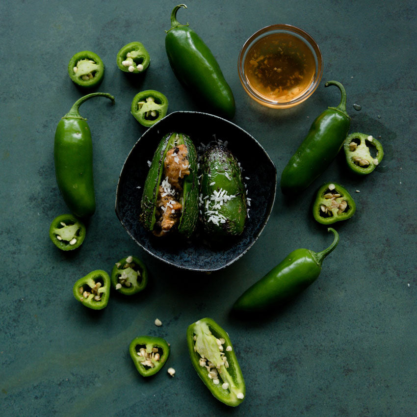 Nadapeno Peppers cooked in a bowl alongside fresh chopped and whole peppers on the side.