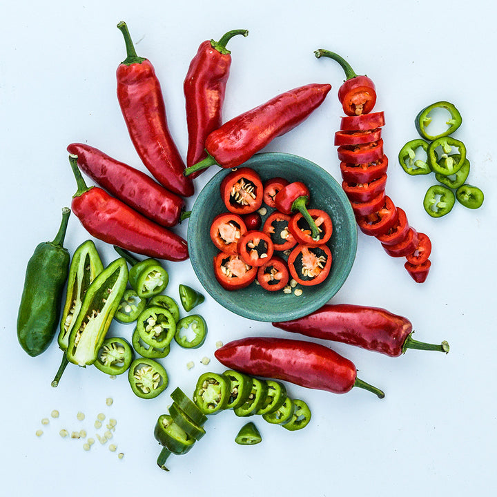 Cut and whole Palmetto Punch Peppers in green and red stage arranged on a white background.