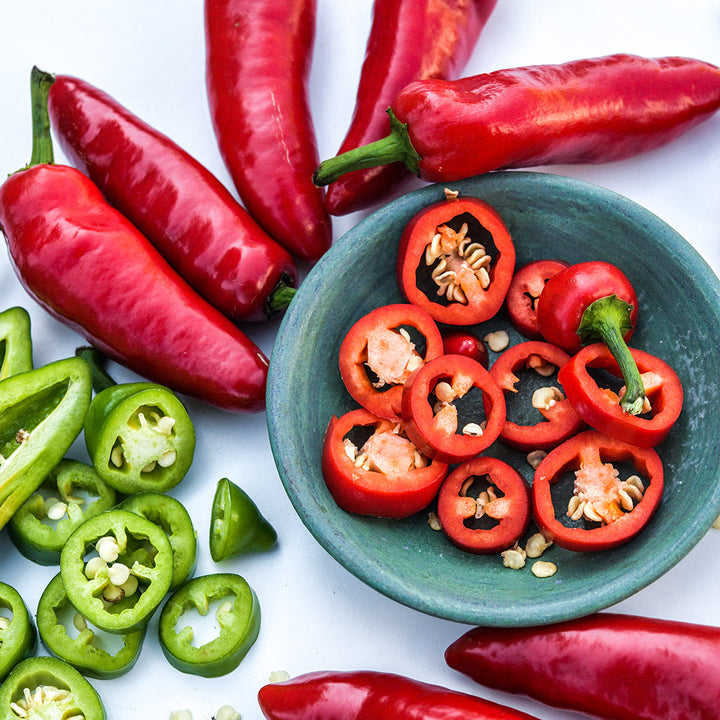 A close-up of whole and cut Palmetto Punch Peppers with cut peppers in blue bowl on a white background.