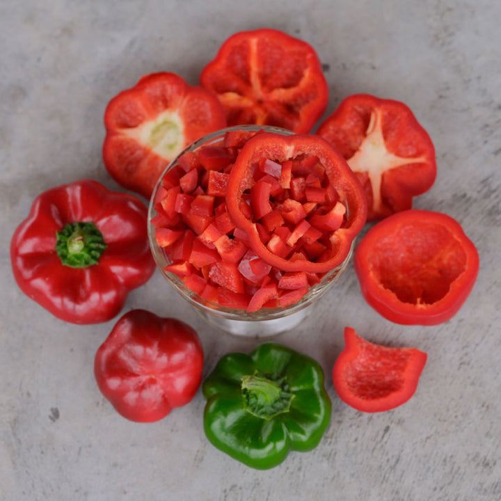Whole red and green Ashe County Pimiento Peppers surround a glass bowl full of diced peppers.