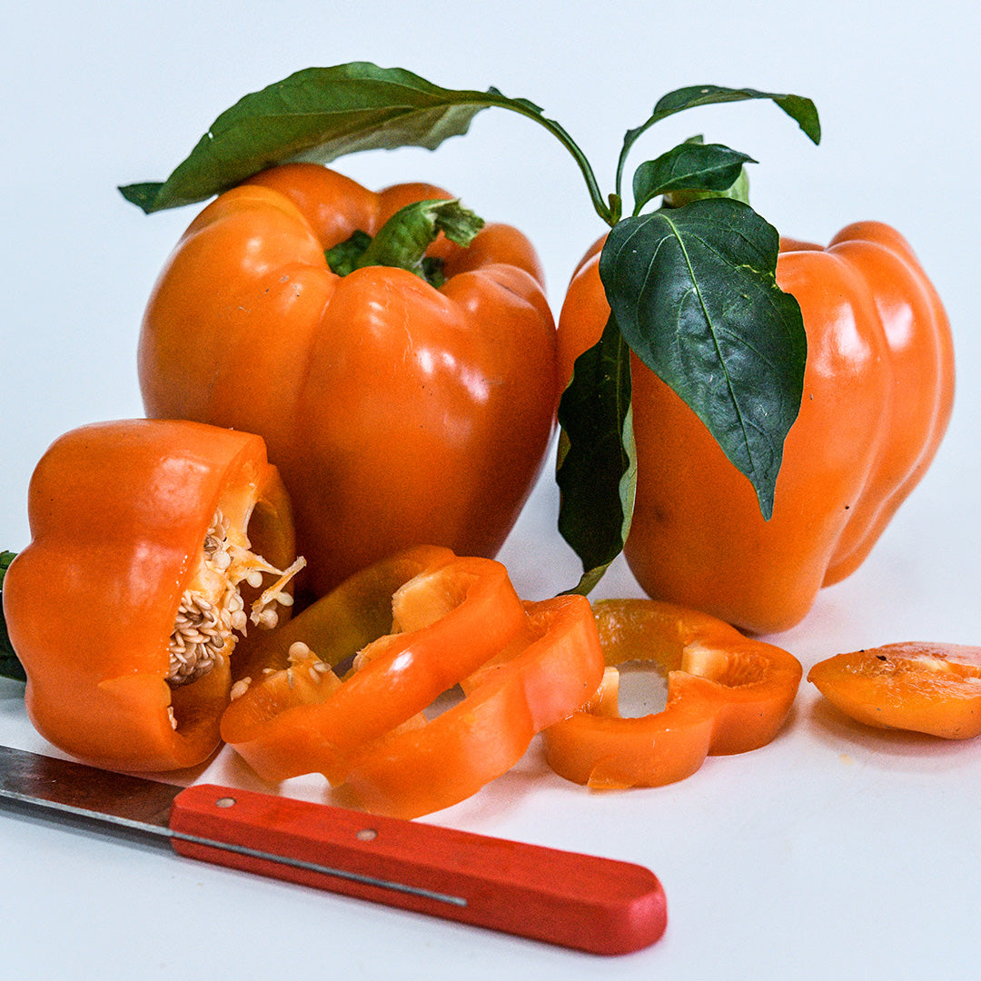 Three Orange Bell Sweet Peppers on a white background. One is sliced into pieces