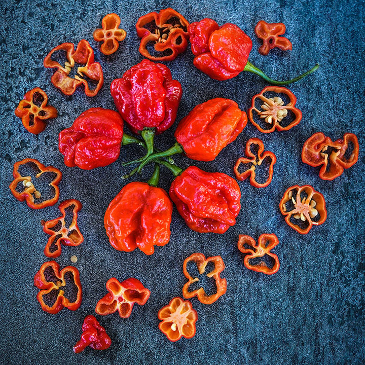 Moruga Sweet Peppers arranged in circle surrounded by slices on a dark stone background.