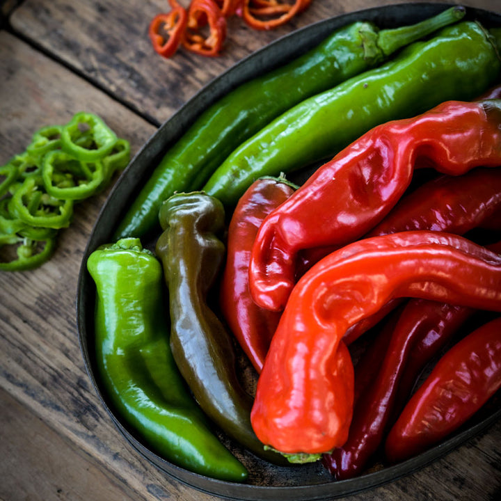 Close-up of red and green Txorixero Peppers in a bowl next to green and red slices on a wooden background.