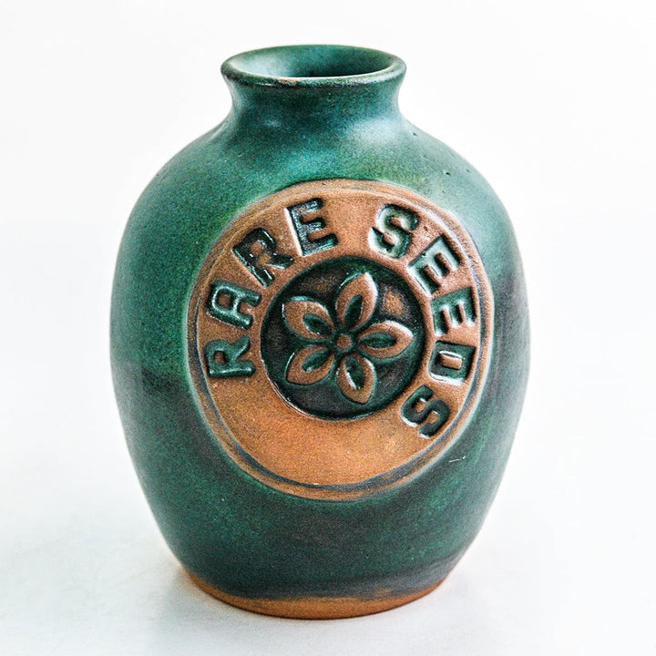 A single greenish blue glazed Handmade Stoneware Pottery Vase with a rareseeds logo on it on white.