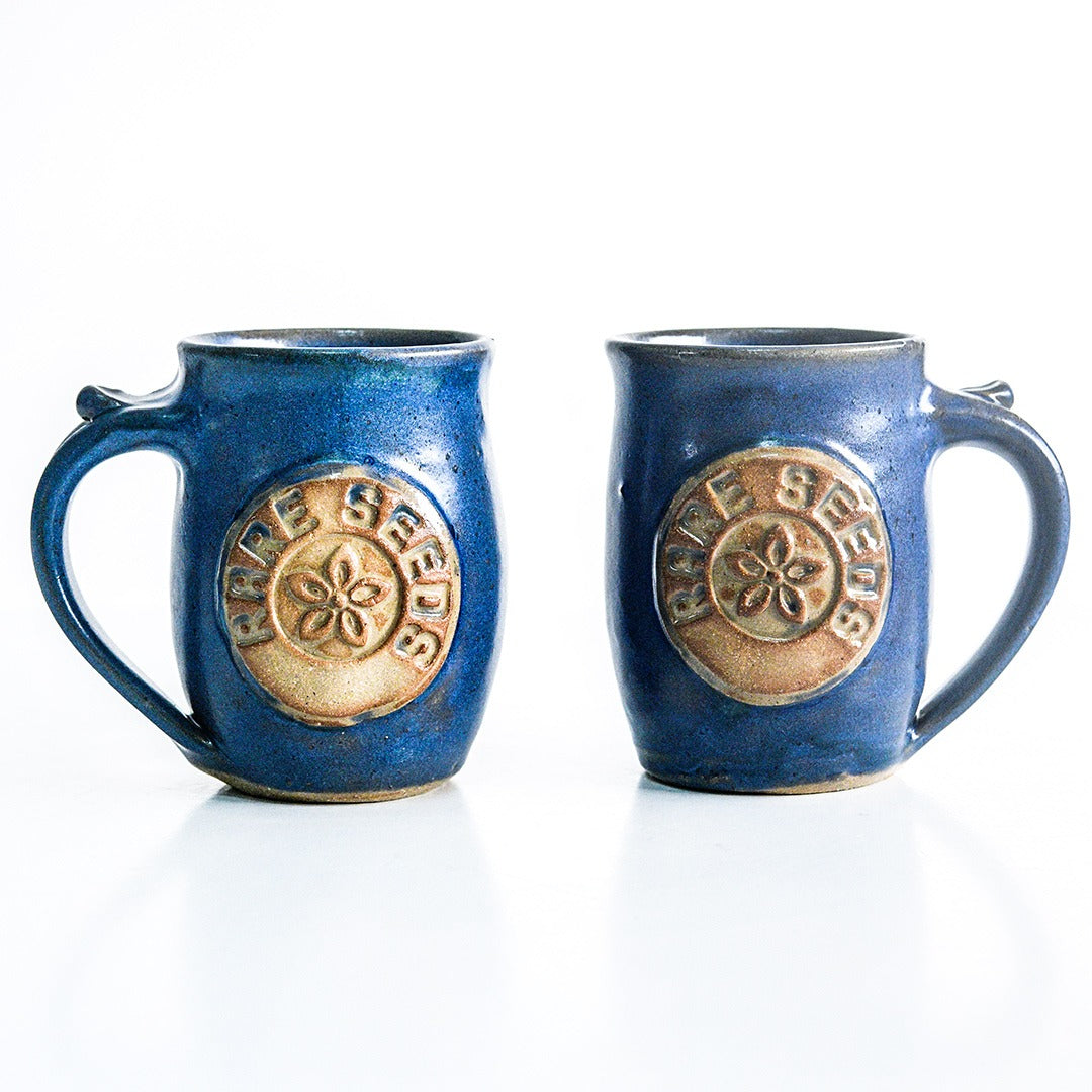 A pair of Handmade Local Mug Blue/Grey Pottery with opposing handles on white.