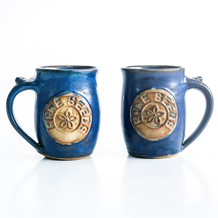 A pair of Handmade Local Mug Blue/Grey Pottery with opposing handles on white.